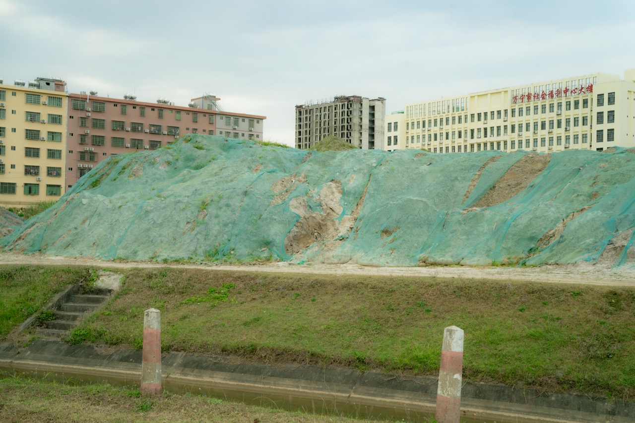 Teal-netted construction mound against urban buildings